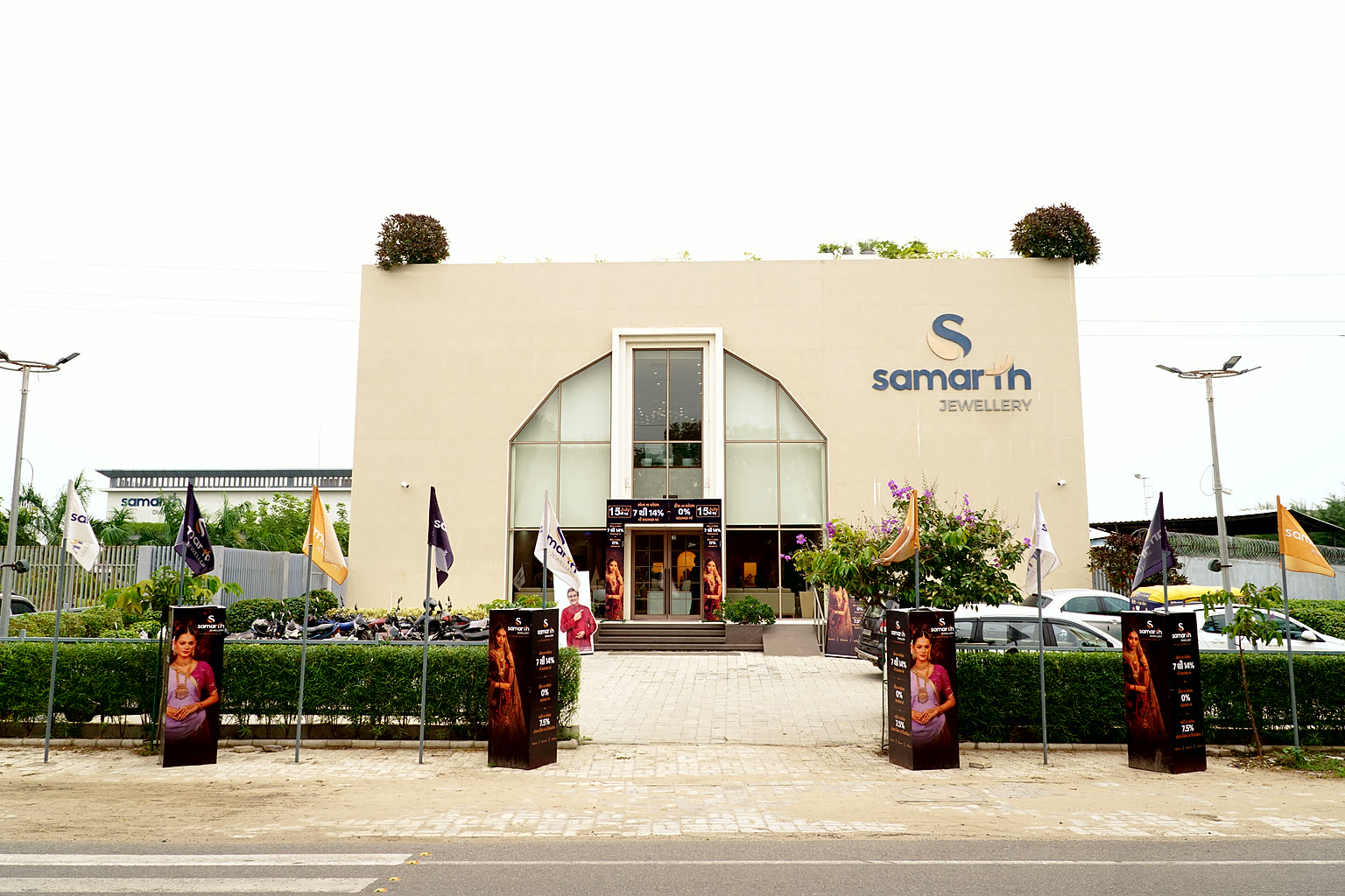 The Samarth Jewellery showroom in Visnagar seen from the road, its arched glass frontage flanked by branded flags.